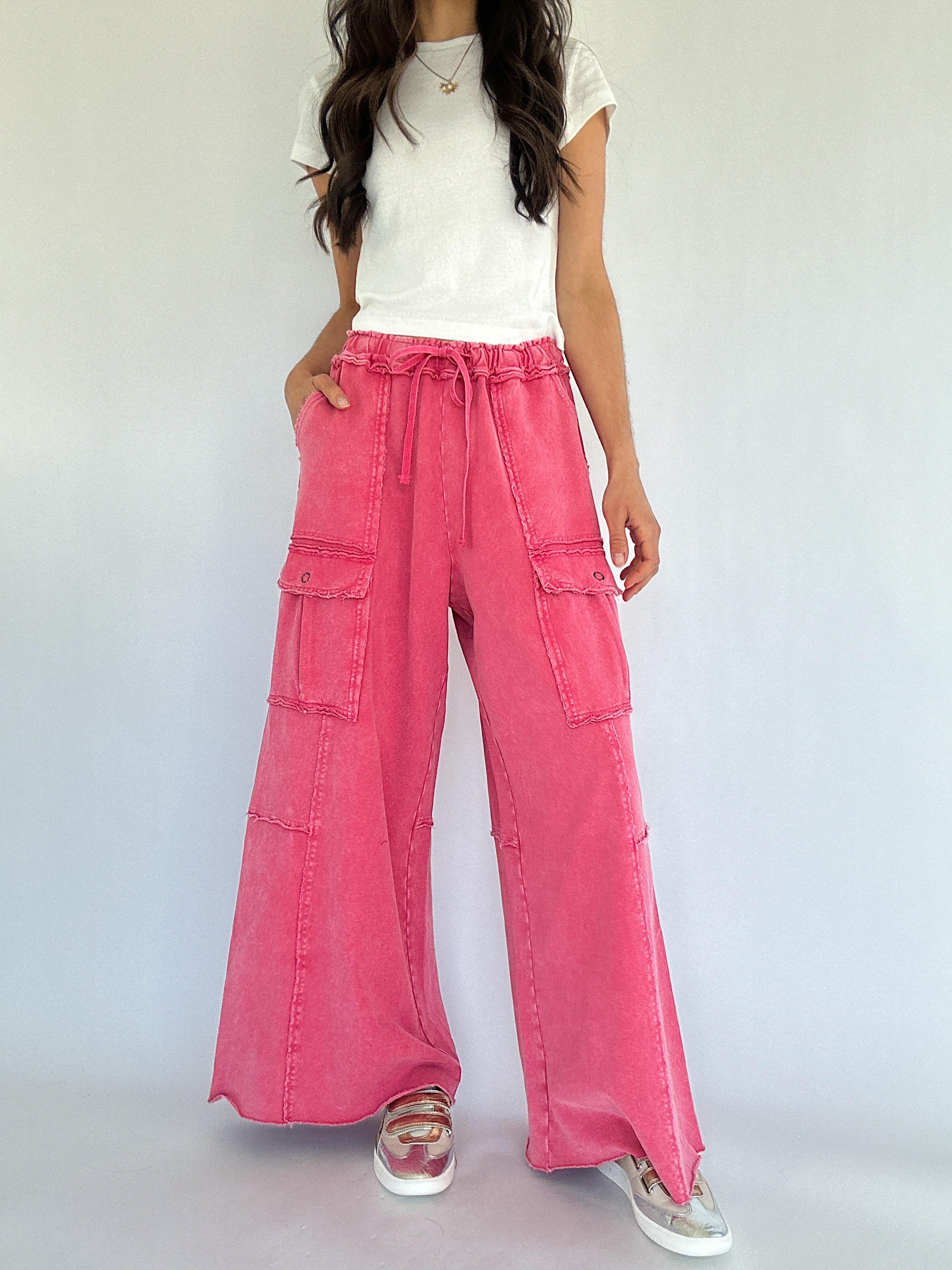 Person wearing pink wide-leg pants with cargo pockets and a white top on a plain background