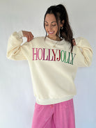Woman wearing a cream sweatshirt with 'HOLLYJOLLY' embroidered text on a white background