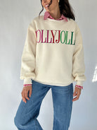 Person wearing a cream sweatshirt with 'HOLLY JOLLY' text, blue jeans, and a checkered shirt on a white background
