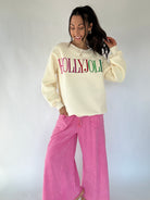 Woman wearing a cream sweatshirt with 'HOLLYJOLLY' text and pink pants against a white background