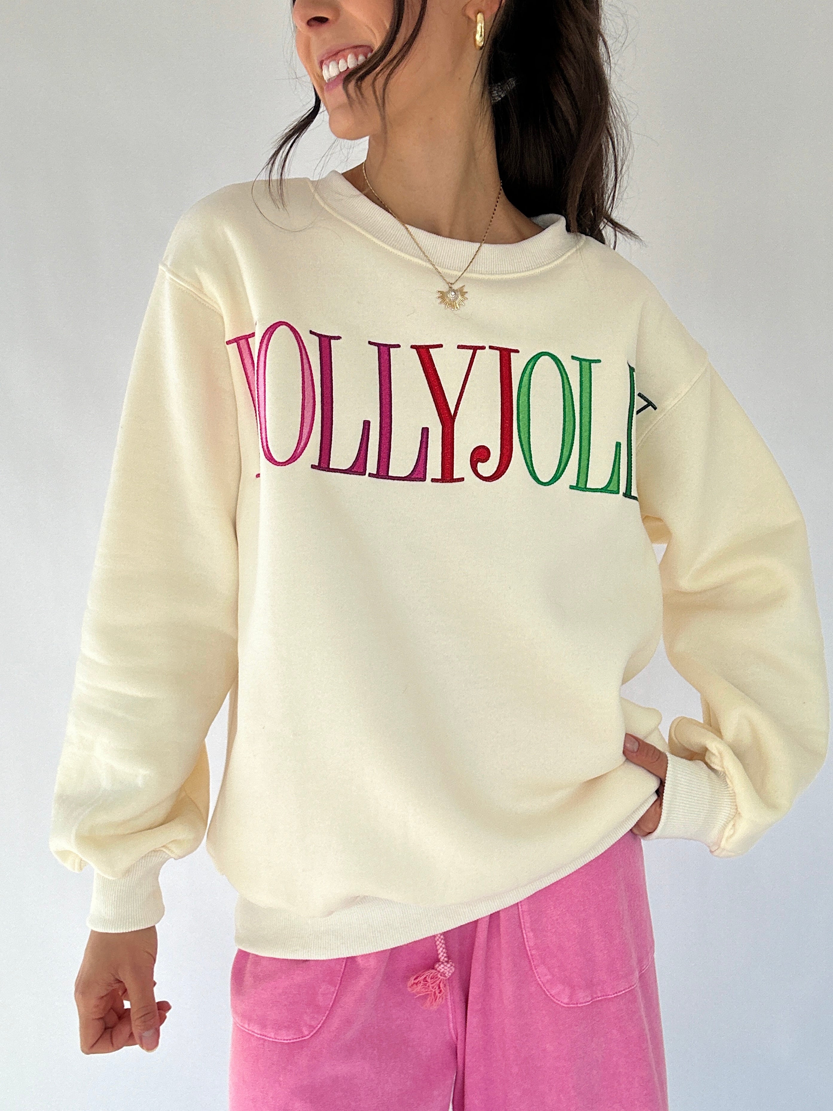 Person wearing a cream sweatshirt with 'Holly Jolly' text, with pink pants against a plain background