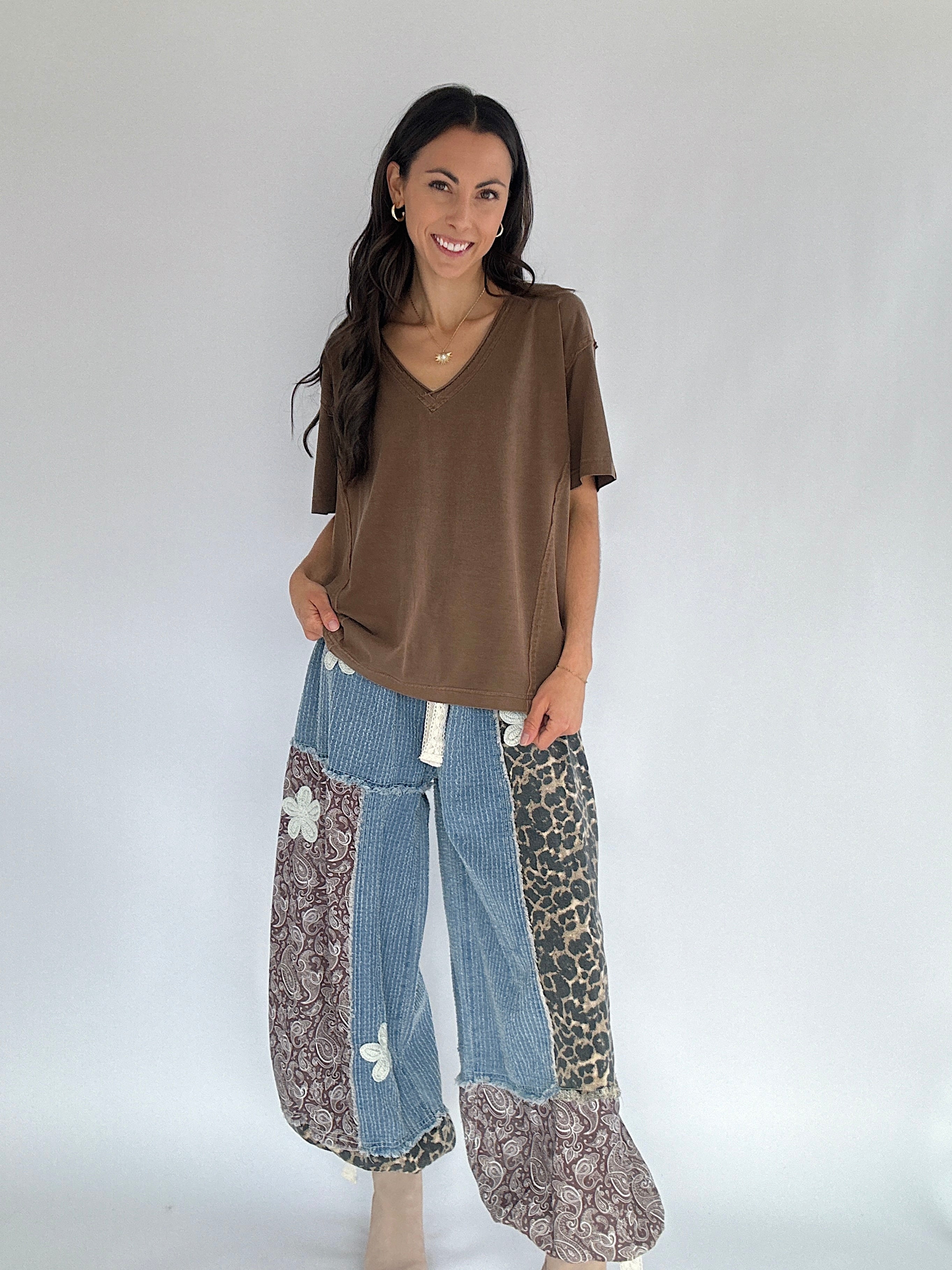 Woman wearing a brown tee and patterned denim and leopard pants on a white background