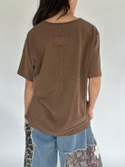 Person wearing a brown oversized t-shirt with a plain background showing back view