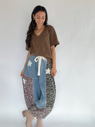 Woman wearing a brown tee tucked into patterned pants with denim accents on a plain background