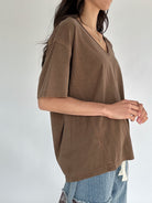 Person wearing a brown t-shirt with a plain background from side