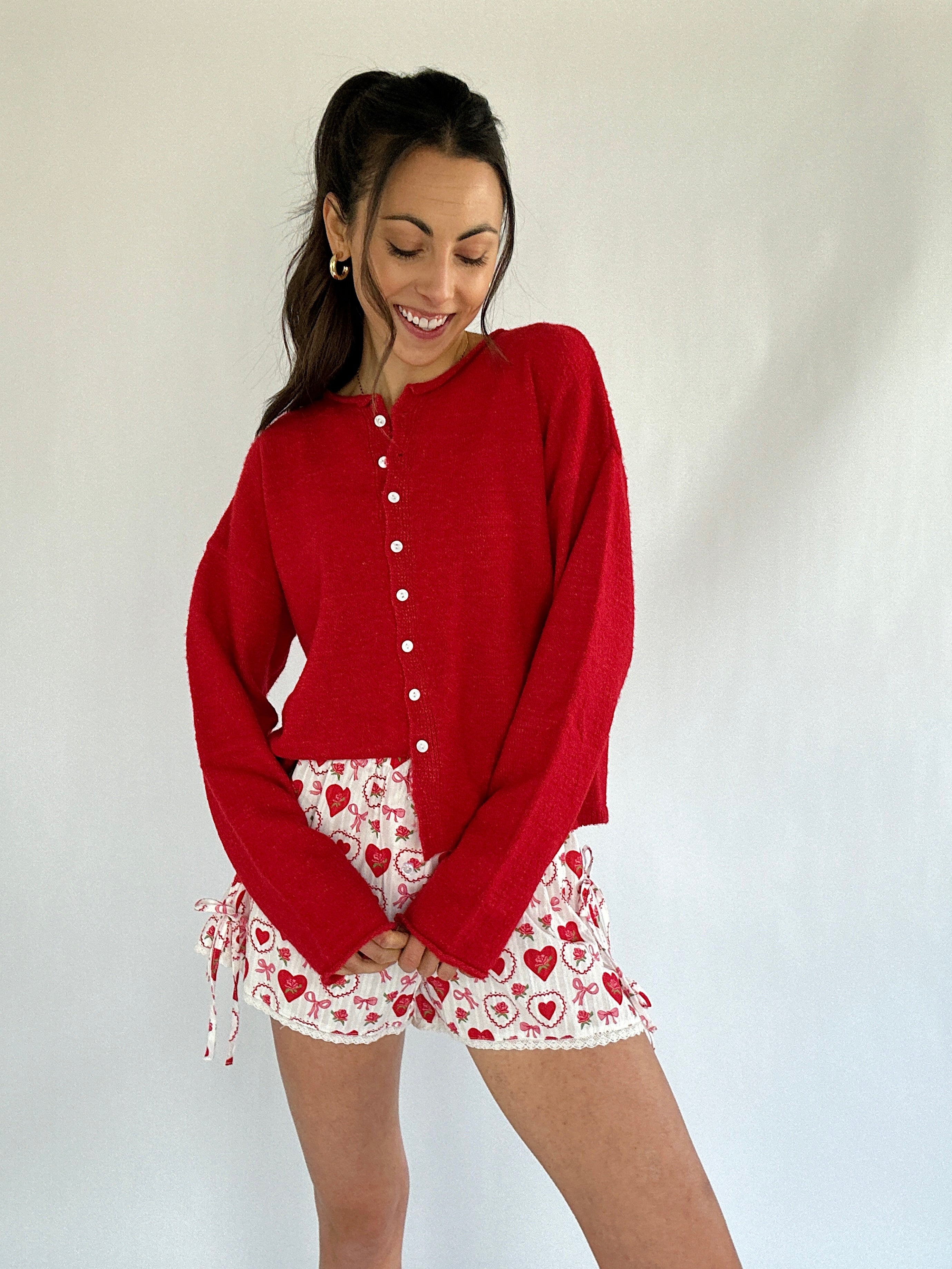 Woman wearing a red cardigan and patterned shorts against a white background