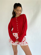 Woman wearing a red cardigan and patterned shorts against a white background