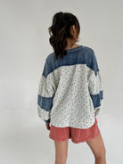 Person wearing a blue and white patterned shirt with rust shorts on a plain background showing back