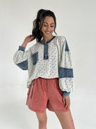 Woman wearing a floral long sleeve top with denim accents tucked into rust red shorts on a white background