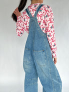 Person wearing a pink candy cane shirt and blue denim overalls on a plain background showing back