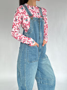 Person wearing a candy cane print cardigan and denim overalls on a plain background showing front patch pockets