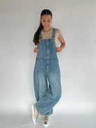 Person wearing blue barrel denim overalls on a plain background