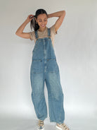 Person wearing blue denim overalls with a barrel silhouette on a plain background