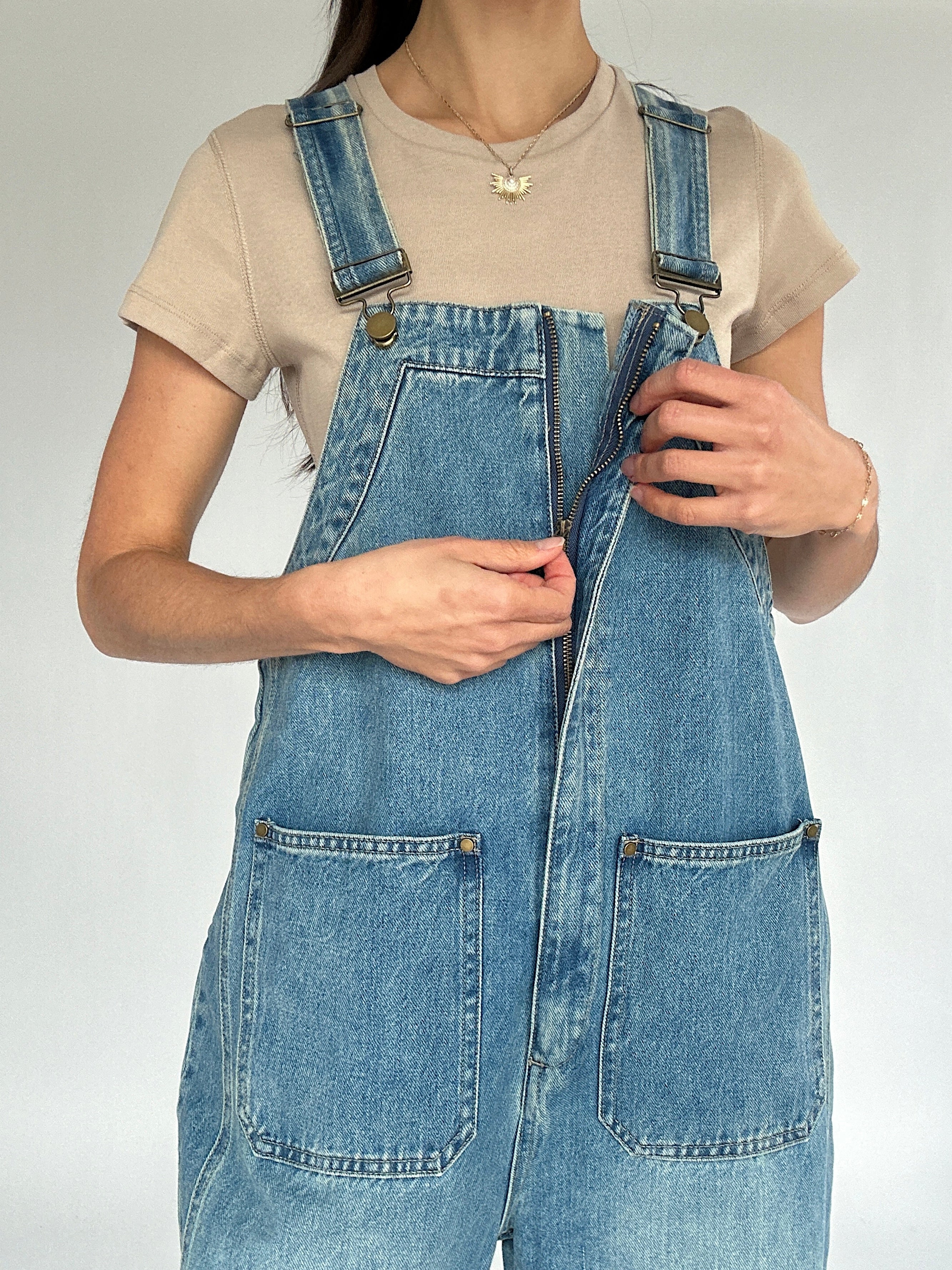 Person wearing a denim overalls with a plain background showing front zipper detail