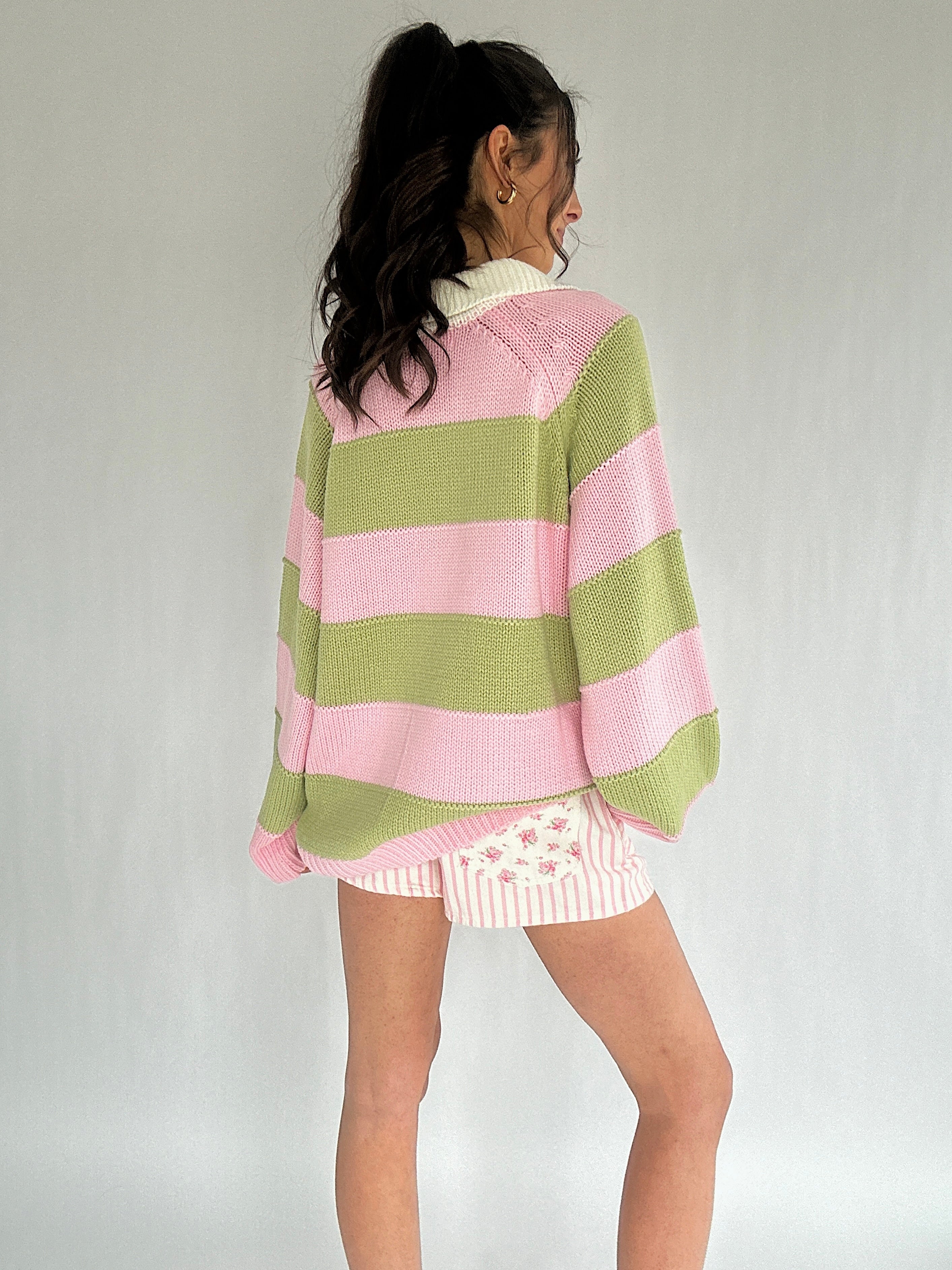 Person wearing a pink and green striped sweater with a white background from back