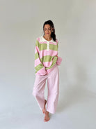 A woman modeling a pink and light green striped henley sweater and matching pink and white gingham wide-leg pants, standing against a neutral light gray studio background.