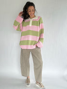 Woman wearing a pink and green striped sweater with checkered pants on a white background