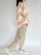 Person wearing a pink and green striped sweater with plaid pants on a plain background from side