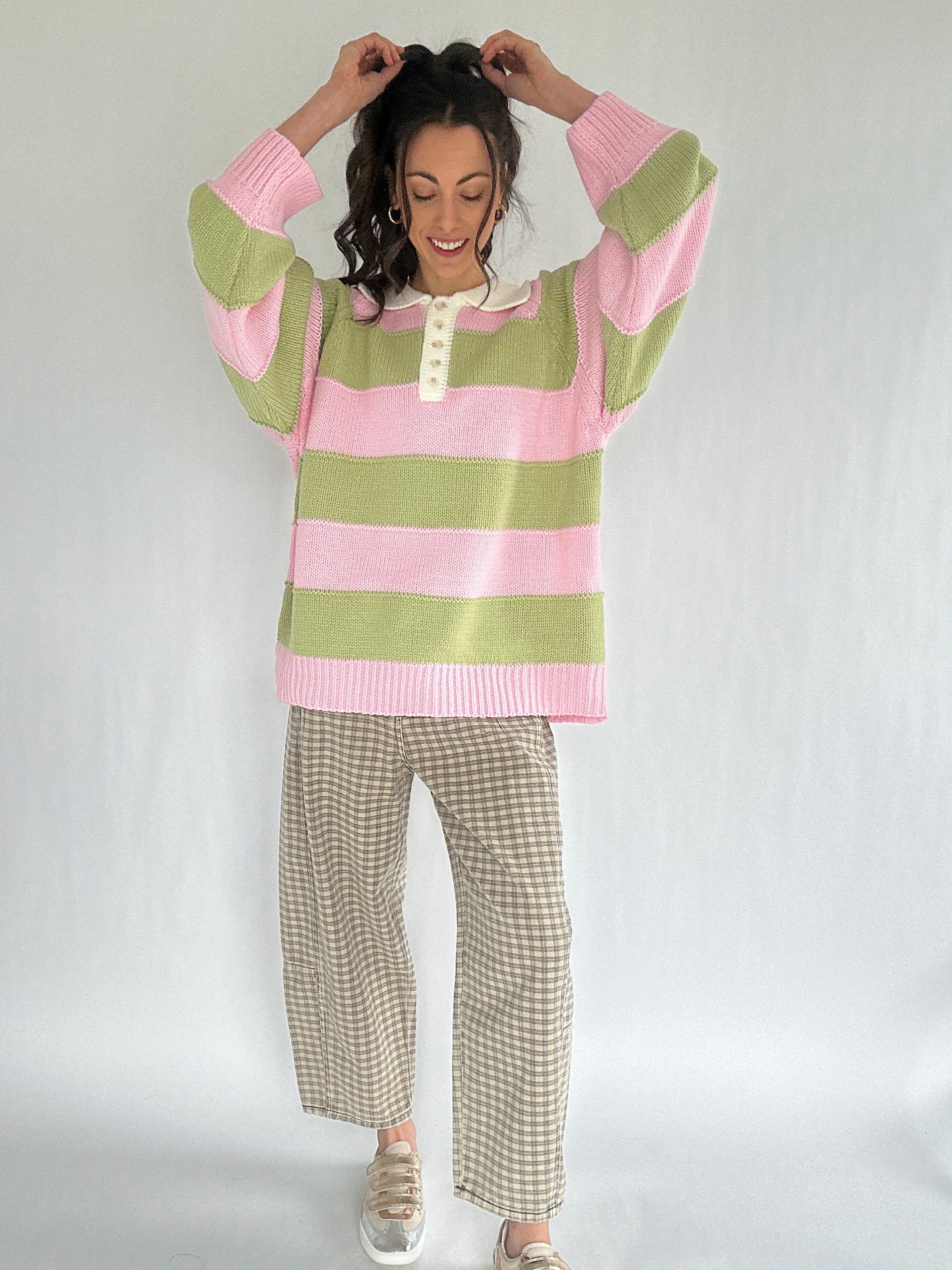Person wearing a pink and green striped sweater with plaid pants on a white background