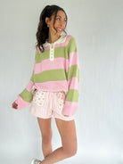 Woman wearing a green and pink striped sweater with white shorts on a plain background