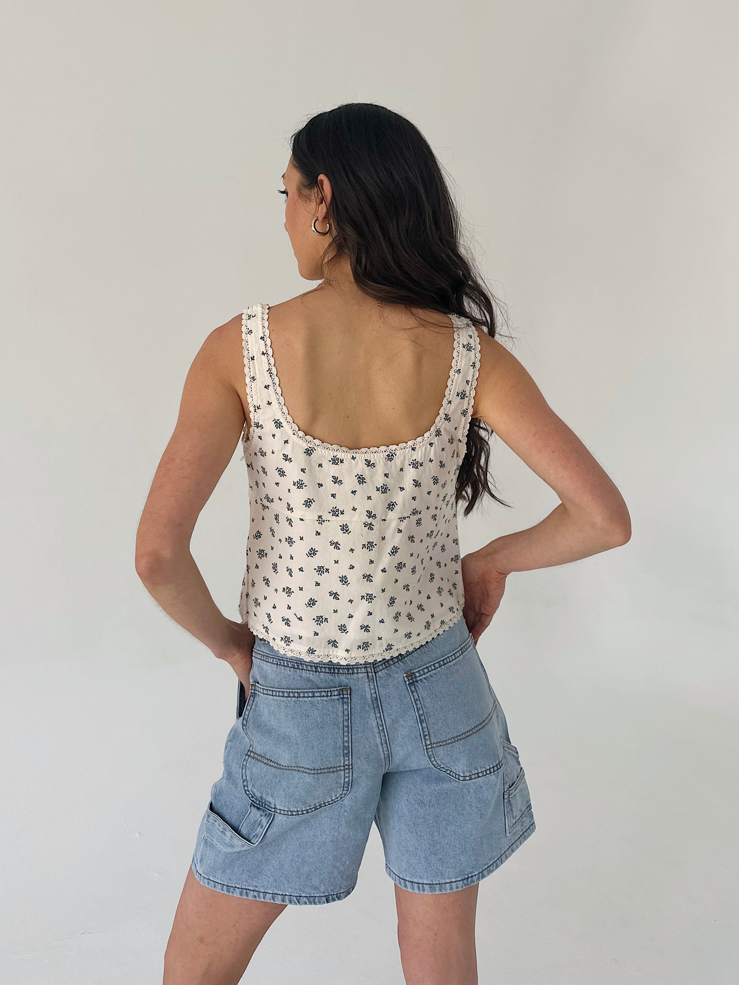 Woman wearing a patterned tank top and denim shorts against a plain background