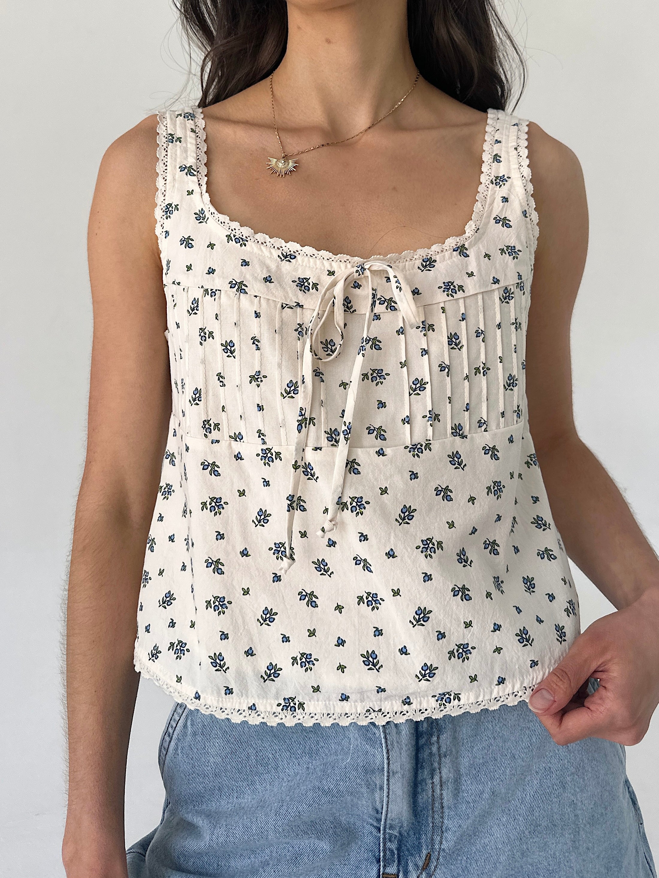 Woman wearing a white floral tank top against a plain background