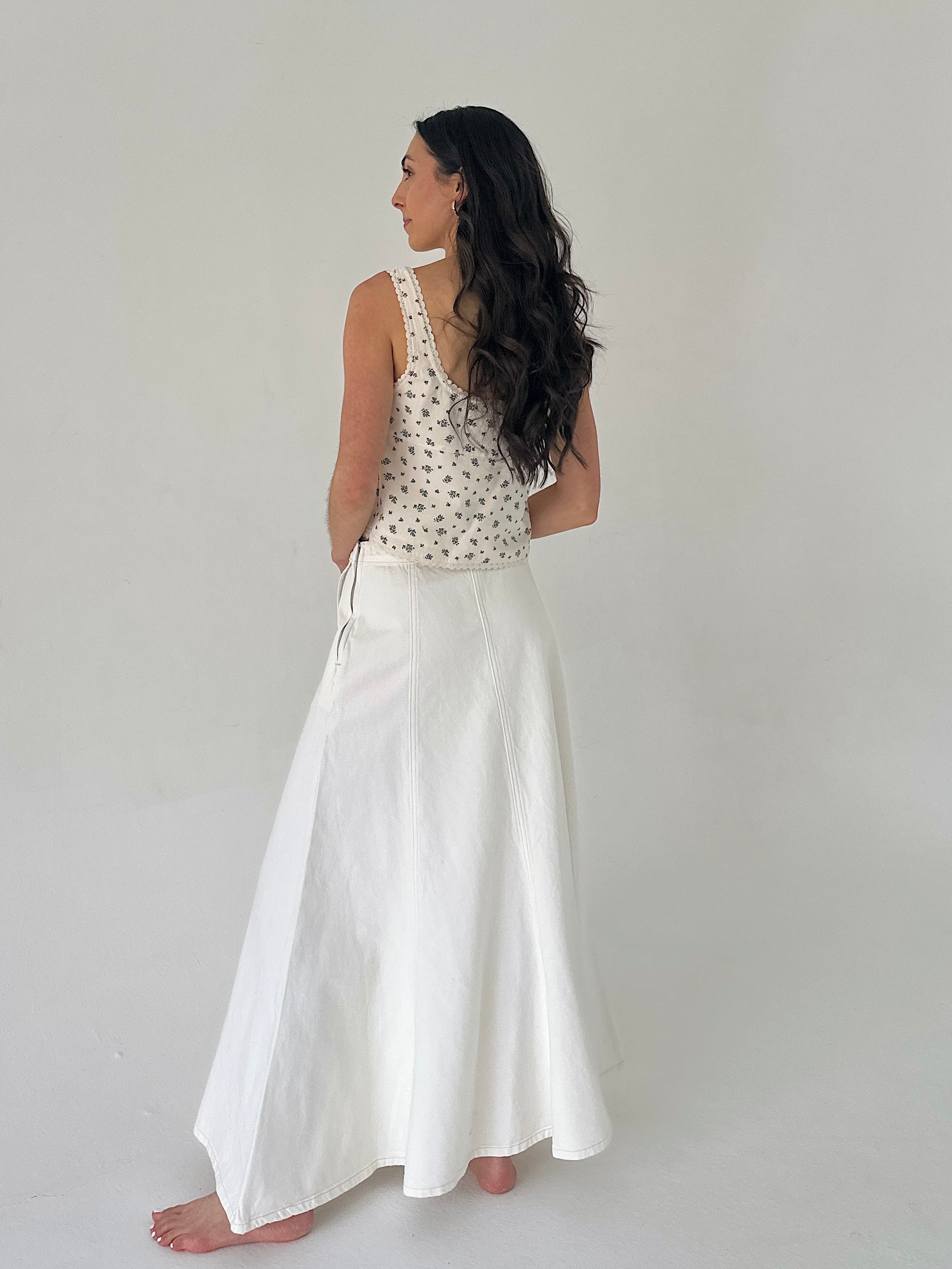 Woman wearing a floral top and white skirt on a plain background showing back