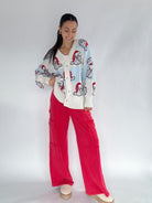 Woman wearing a Santa face patterned cardigan and red pants on a white background