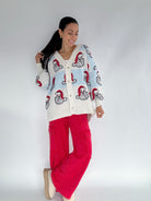 Woman wearing a white cardigan with red and blue stripe and Santa face pattern and red pants on a white background