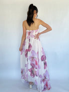 Woman wearing a strapless floral dress against a white background from back