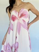 Woman wearing a strapless floral dress with pink and purple flowers on a light background showing notched neckline