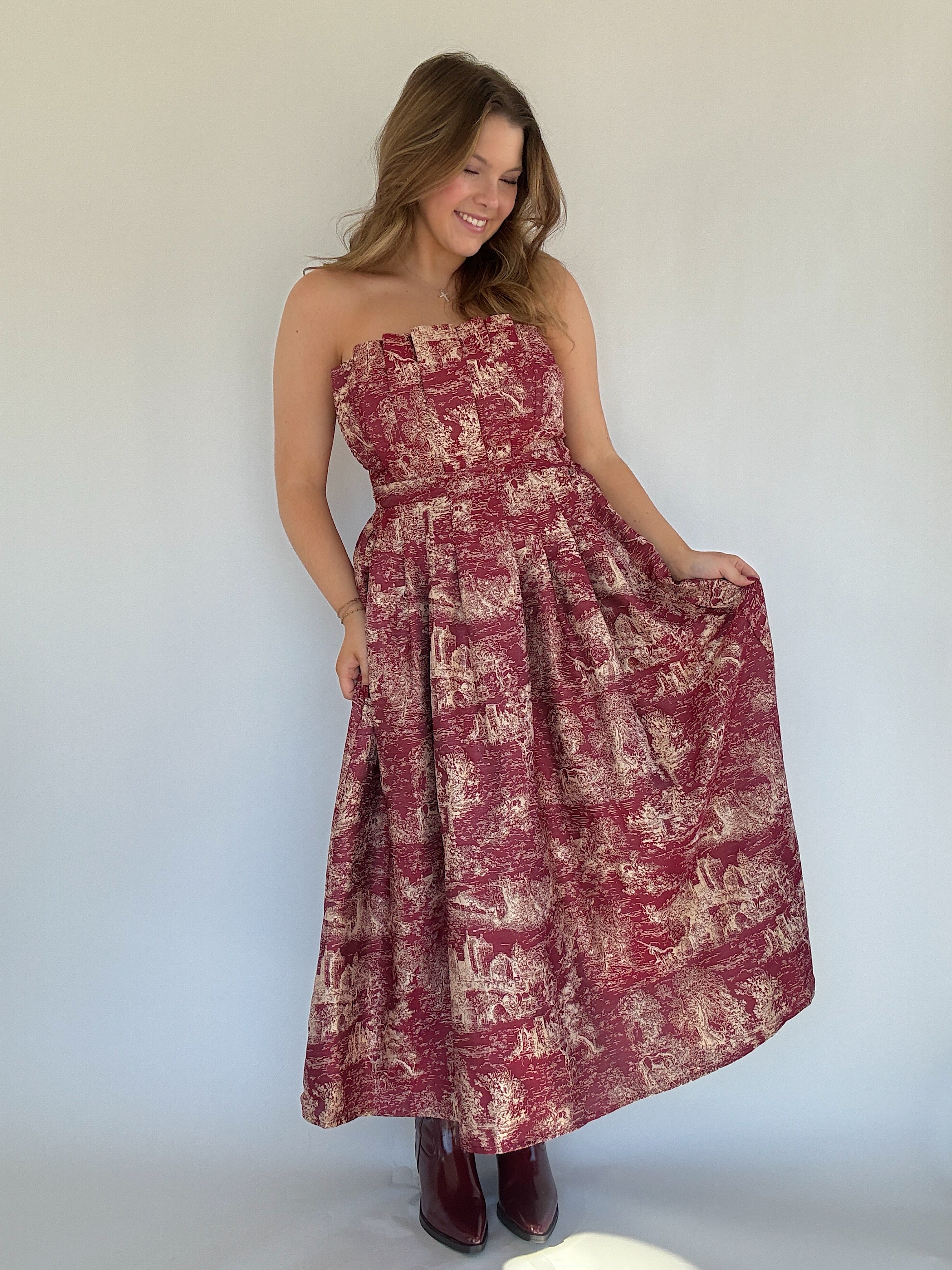 Woman wearing a burgundy strapless toile dress against a plain background