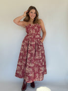 Woman wearing a red toile floral dress against a white background