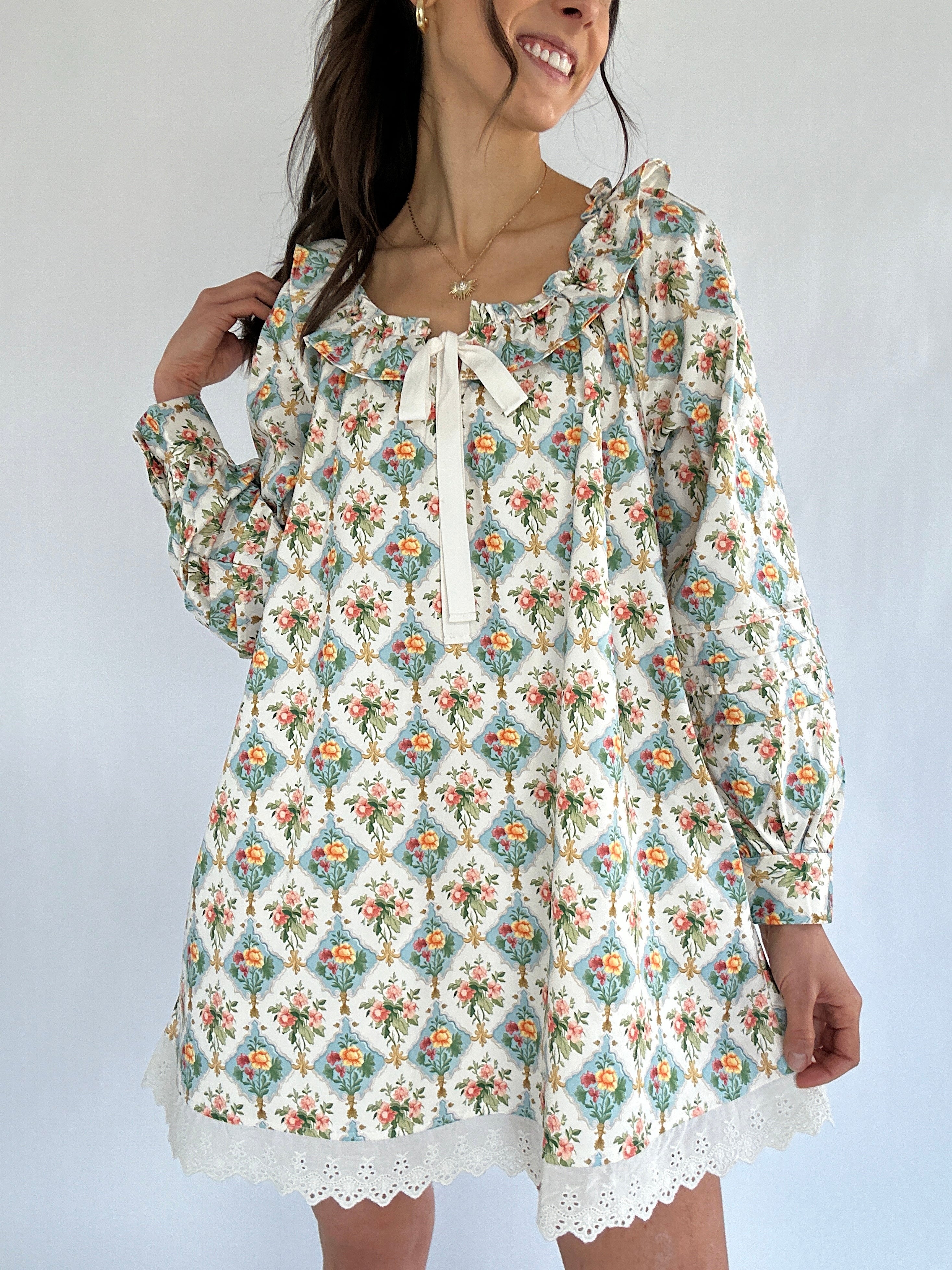 Woman wearing a floral mini dress with long sleeves and lace trim against a white background