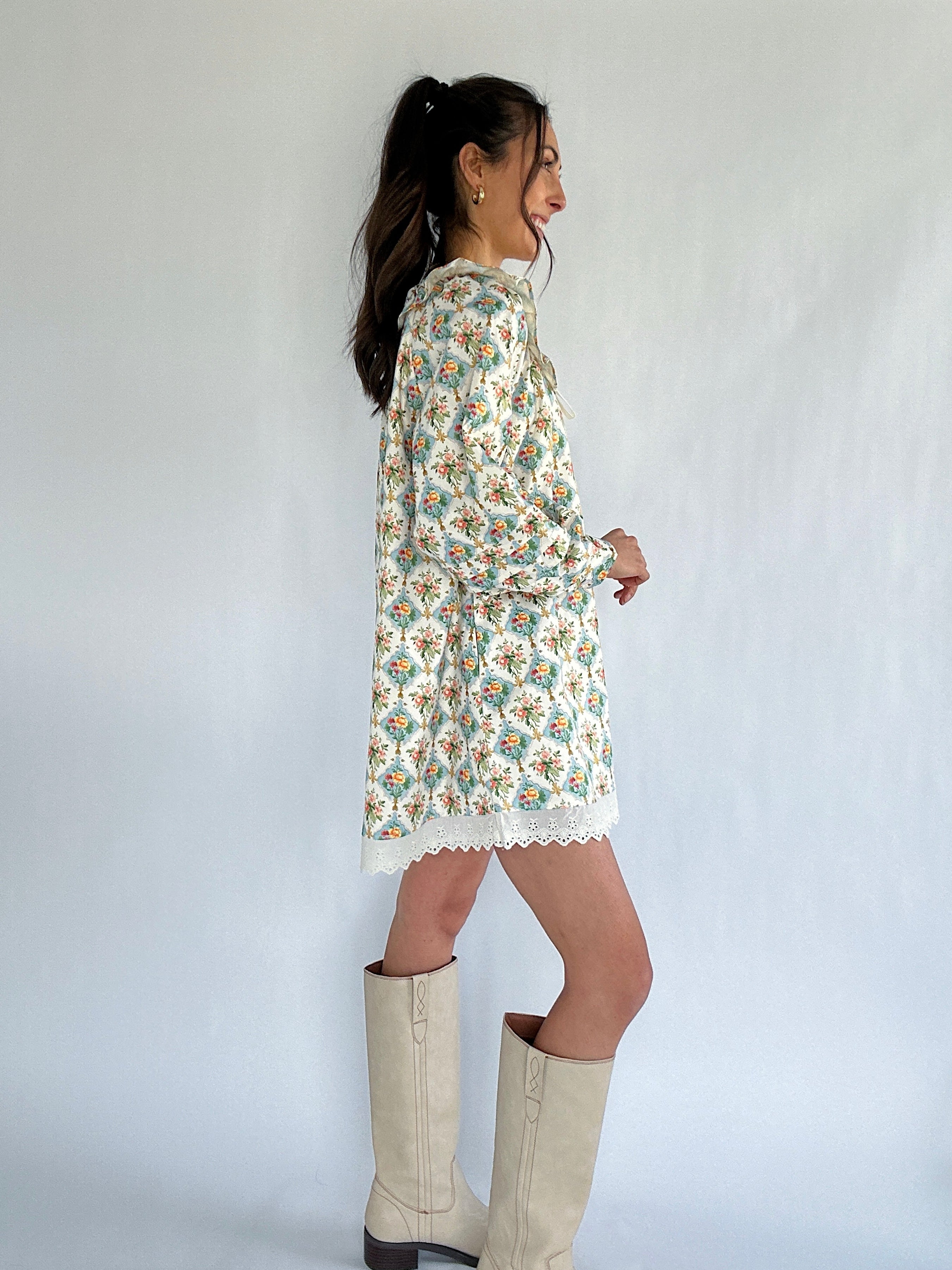 Woman wearing a floral dress and white boots against a plain background showing the side