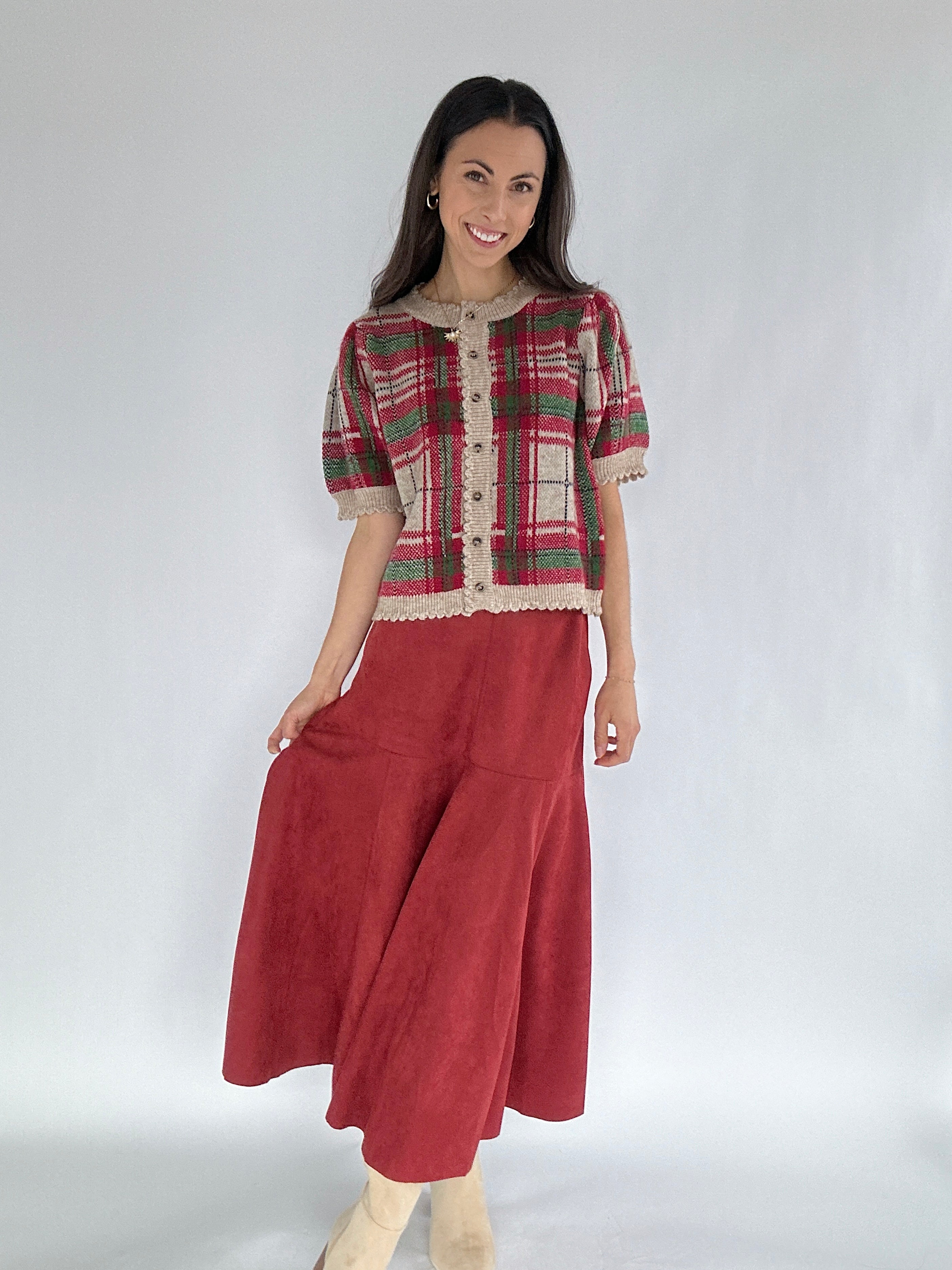 Woman wearing a red and green plaid sweater top with a red suede skirt on a white background