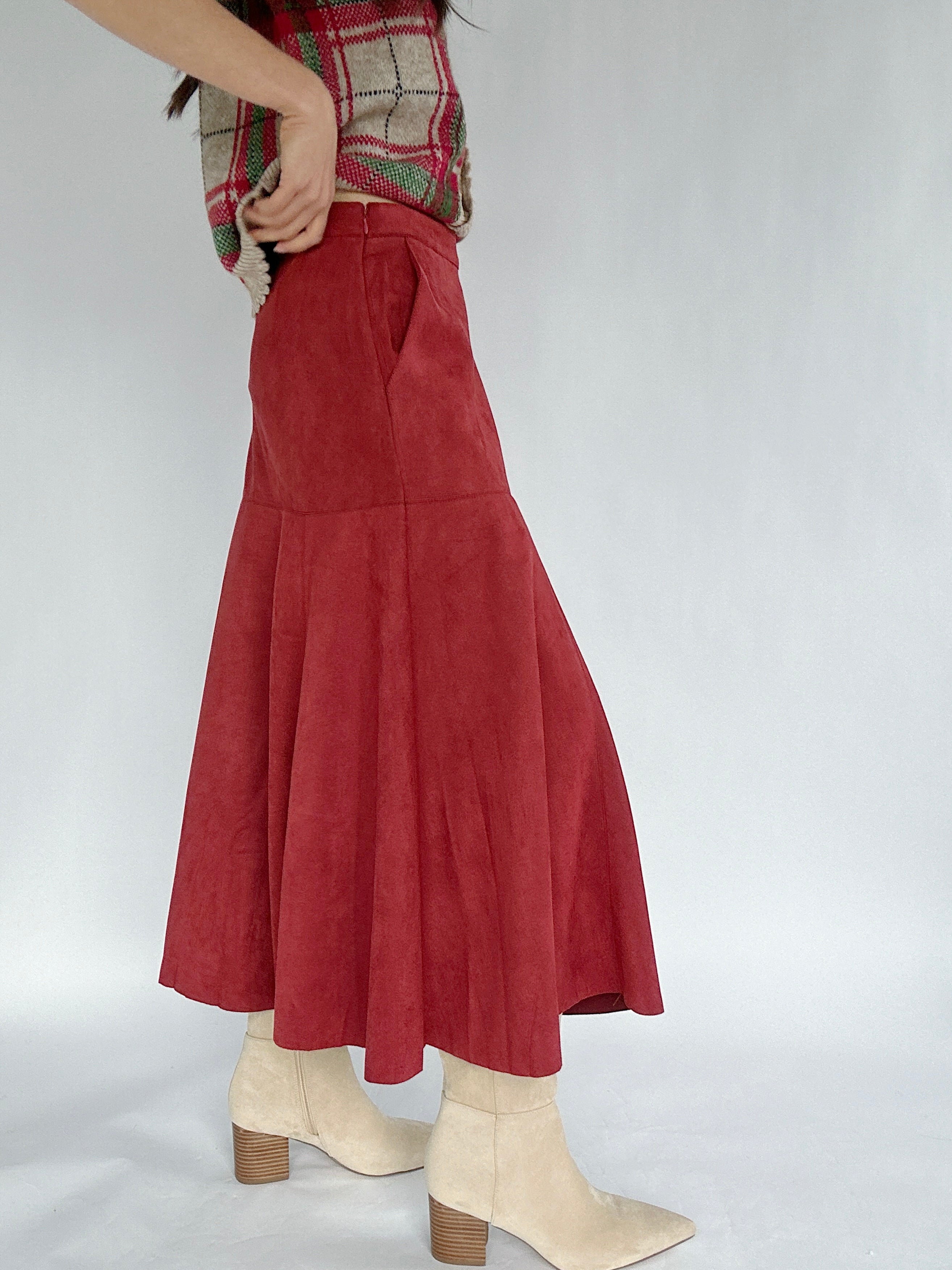 Person wearing a red suede skirt with a plain background showing side pockets and side zipper