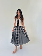 A woman modeling a sleeveless knit vest with a black and white gingham plaid skirt, standing against a plain off-white studio background.
