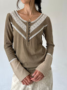 A woman wearing a ribbed long-sleeve henley top in taupe olive with white lace trim and button details, paired with a light patterned skirt against a plain light gray background.