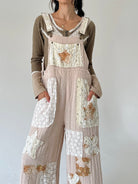 A person wearing a beige and brown patchwork overall jumpsuit with lace and floral applique details, layered over a green long-sleeve shirt, against a plain light gray background.