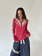 A woman modeling a long-sleeve henley top in dusty rose pink with cream lace trim, paired with dark blue wide-leg pants with lace details, against a plain off-white wall.