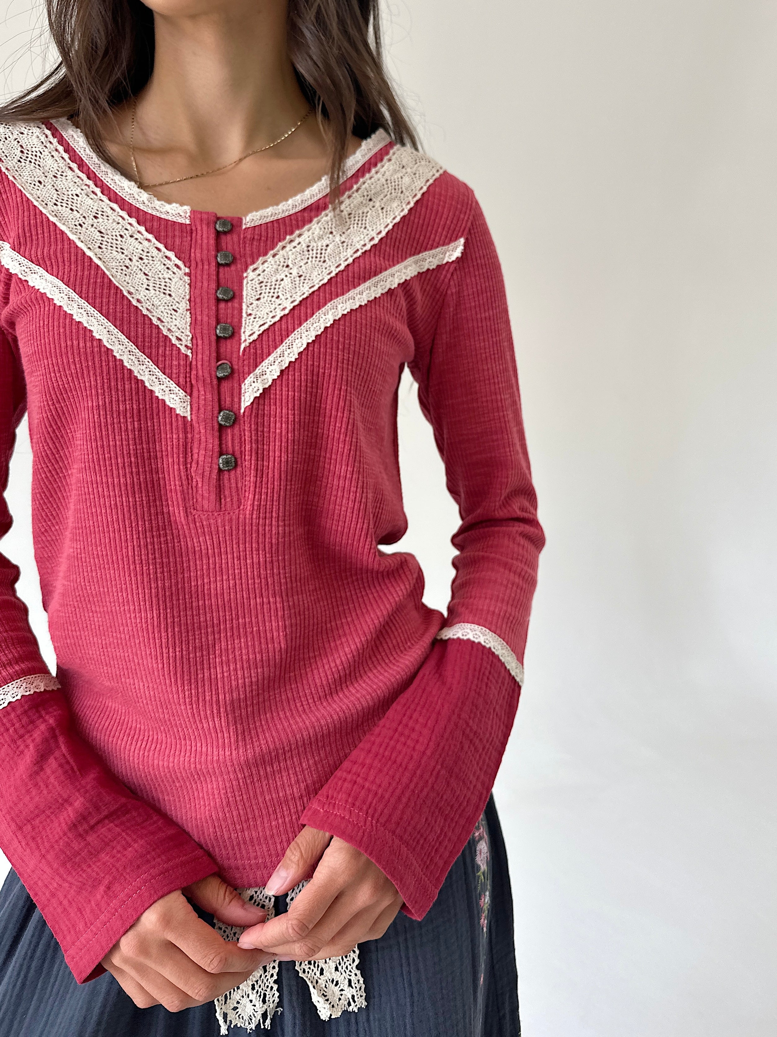 A woman wearing a long-sleeve knit henley top in dusty rose pink with cream lace trim and dark buttons, paired with a dark skirt.
