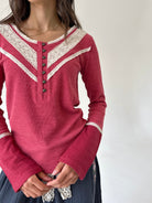 A woman wearing a long-sleeve knit henley top in dusty rose pink with cream lace trim and dark buttons, paired with a dark skirt.
