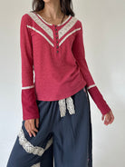 A woman wearing a long-sleeve knit top in dusty rose pink with cream lace trim along the V-neckline and cuffs, paired with dark blue wide-leg pants featuring cream lace details.