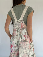 Person wearing a green top and floral overalls against a white background showing back