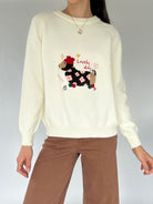 Person wearing a cream sweater with a dog design that says 'lovely day' and brown pants on a gray background