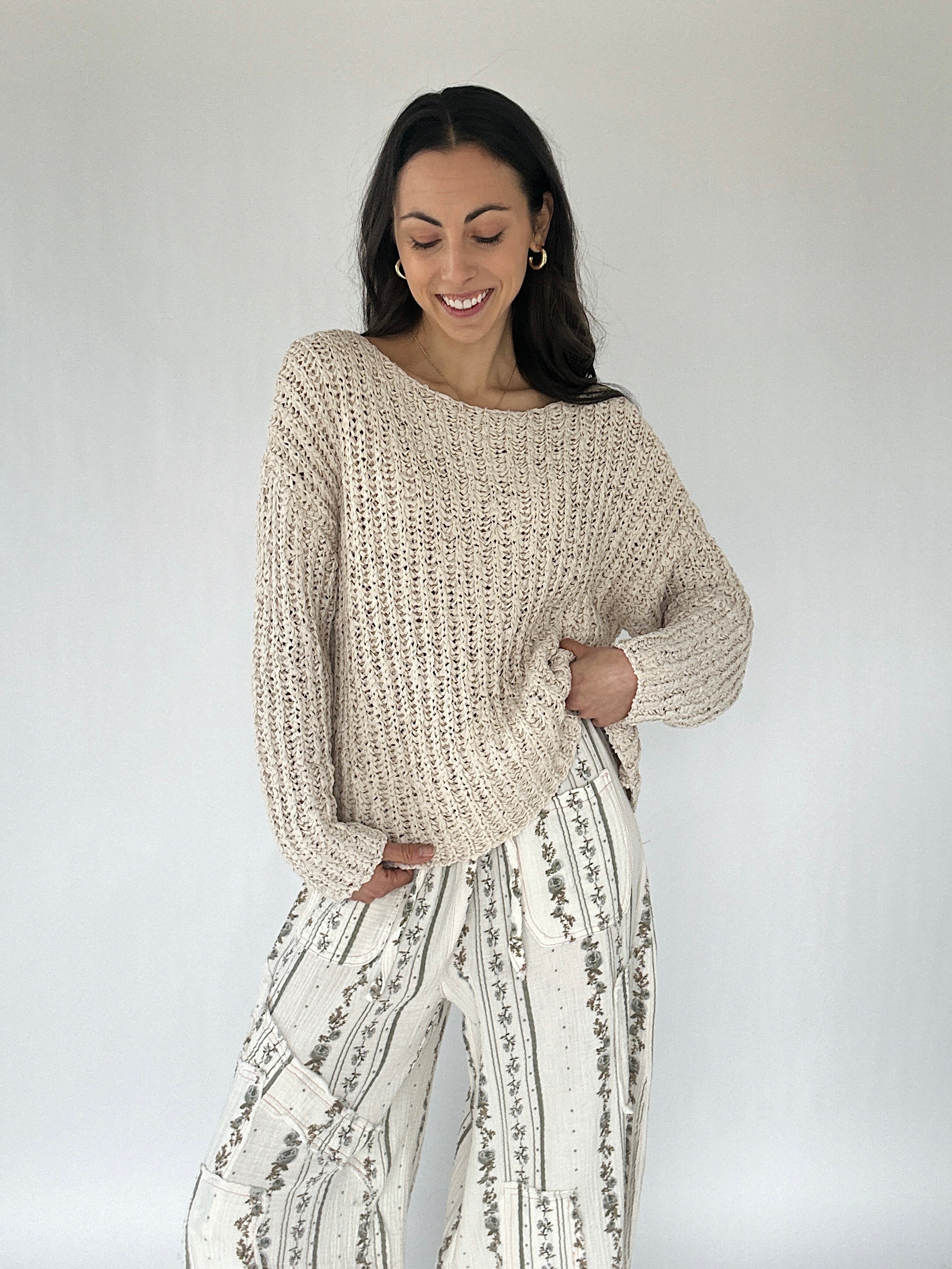 Woman wearing a beige knitted sweater and patterned pants against a white background
