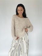 Woman wearing a beige knitted sweater and patterned pants against a white background