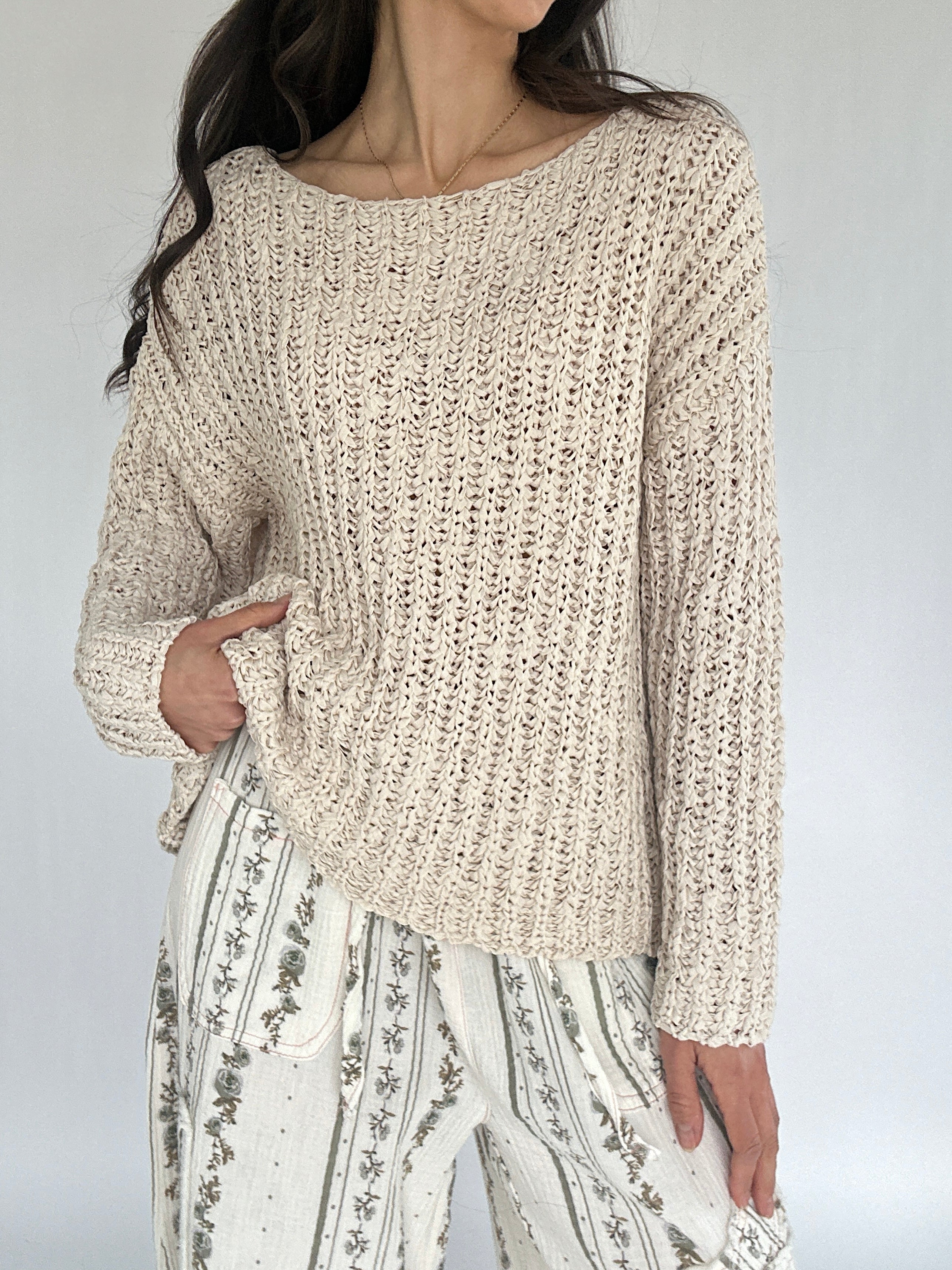 Person wearing a beige knitted sweater and patterned pants against a plain background