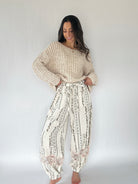 Woman wearing a beige knit sweater and patterned pants against a white background